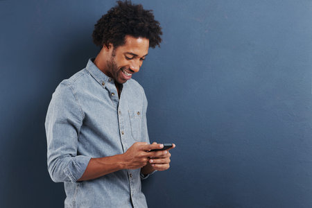 Connected to his circle of friends. a handsome young man using a mobile phone on a gray background.