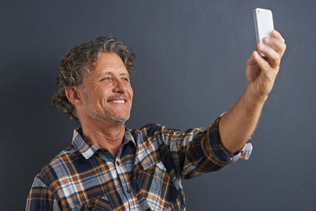 A selfie for the kids. A happy mature man taking a picture of himself with his smart phone.の写真素材