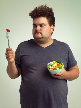 This is just not going to happen. Studio shot of an overweight man holding a bowl of salad.