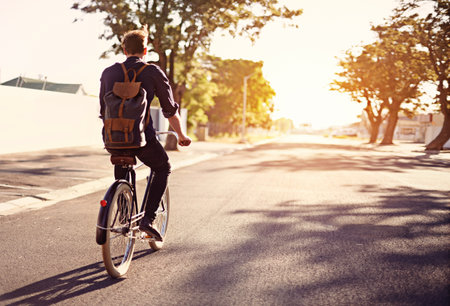 Taking a ride on the brighter side of life. Rearview shot of a young man riding a bicycle outdoors.の写真素材