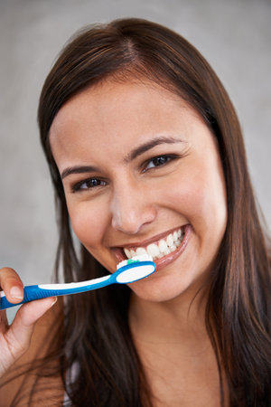 Brushing bad breath away. An isolated portrait of a young woman happily brushing her teeth.の写真素材