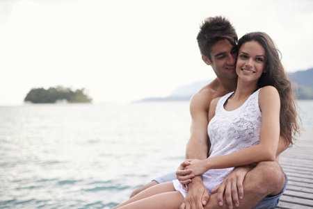 Enjoying some privacy on the pier. an affectionate young couple sitting together on a jetty.の写真素材