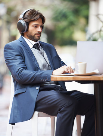 My favorite songs always increase my productivity. A businessman wearing headphones and working on his laptop at a coffee shop.の写真素材