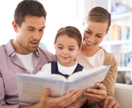Stories that everyone can enjoy. young parents reading a book with their daughter as they sit on the sofa.の写真素材