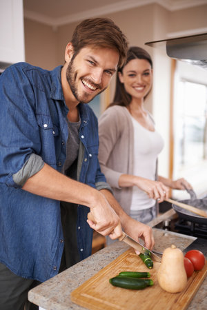 Doesnt make him uncomfortable at all. A young couple making dinner together at home.の写真素材