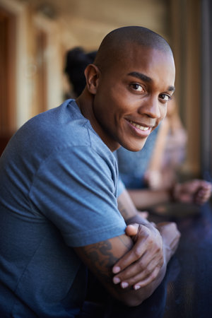 Its the student life for me. A portrait of a happy young man sitting in a bar with friends.の写真素材