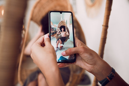 Hands, phone and fashion with a designer taking a photograph of a model black woman in a swing chair. Smartphone, photography and style with an edgy female on screen or display of a design employeeの写真素材