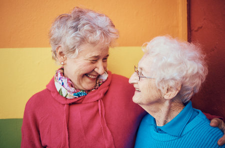Friends, happy and retirement with a senior woman and friend outdoor together on a color wall background. Smile, freedom and glasses with mature female friendship bonding or laughing outsideの写真素材