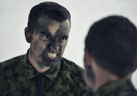 Ready for war. A military man with his face camouflaged making a mean face while looking in the...