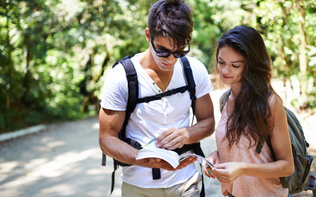 Which way should we go. a young couple looking at a guidebook while out hiking.の写真素材