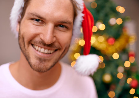 Filled with Christmas cheer. A handsome man smiling at the camera with a decorated christmas tree in the background.の写真素材