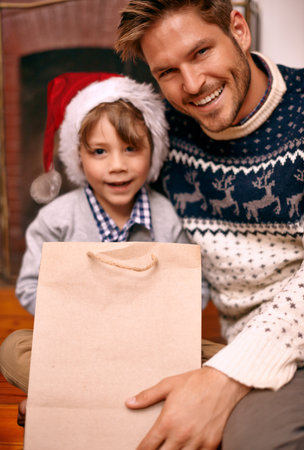 Time for presents. A boy and his dad sitting with a gift on Christmas eve.の写真素材
