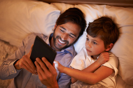 Modern bedtime story. A father reading a bedtime story to his son from an e-reader.の写真素材
