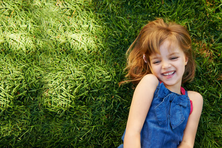 Sunny day fun. a cute little girl smiling while lying down on grass.の写真素材