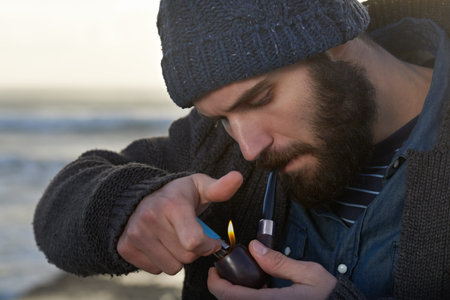 Smoking a pipe. a bearded man smoking a pipe outside.