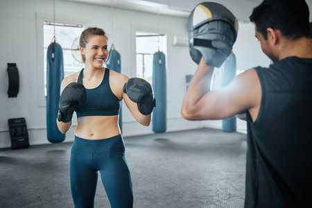Boxing gym, combat sport and woman training for fight, exercise and workout in fitness club. Happy female, strong athlete and smile sports people fighting with personal trainer, coach and kick boxerの写真素材