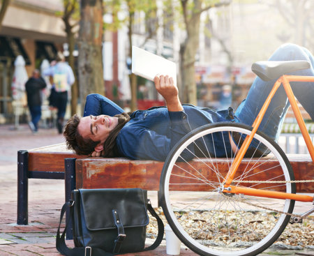 Take a break in an urban space. a man using his tablet while taking a break in the city with his bicycle beside him.の写真素材