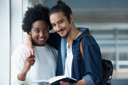Their life long love started at College. Portrait of a college couple holding hands with a text book in front of them.の写真素材