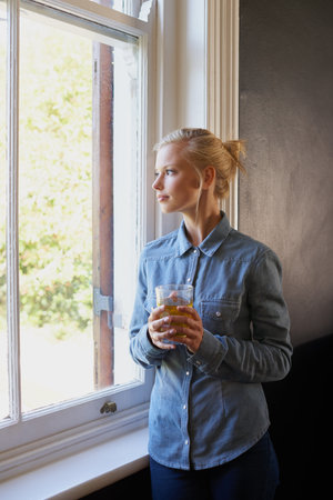 Having a relaxed day at home. A young woman drinling tea while standing at her window.の写真素材