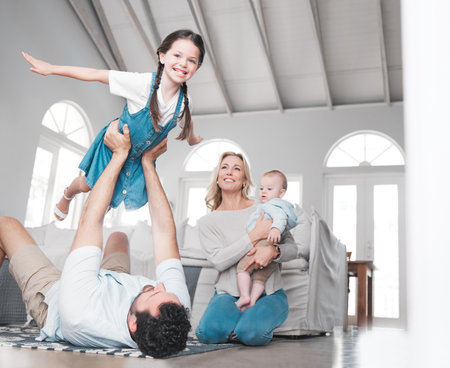 Father, play game and girl in the living room with baby and mom on the floor in house. Trust, love and support as happy child having fun or fly, care and joy with her family in home lounge togetherの写真素材