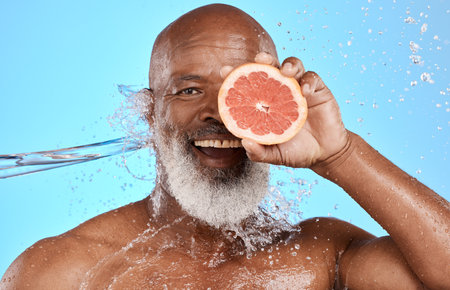 Grapefruit, portrait and senior black man in studio with water splash for bathroom product, skincare and vitamin c health promotion. Smile face, fruit and an african elderly model with facial glowの写真素材
