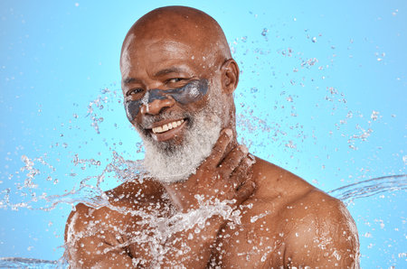 Skincare, water and portrait of black man with facial on blue background in studio for wellness, spa and cleanse. Cleaning, beauty and senior male with water splash, facial mask and luxury treatmentの写真素材