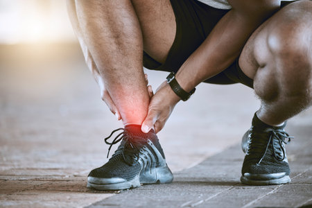 Sports, injury and fitness ankle pain during exercise, running and training outside with red color on foot, muscle or joint. Man, risk and hurt hands athlete holding broken leg bone with bad bruiseの写真素材