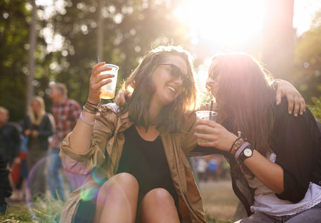 They go together like brandy and lemonade. two young friends enjoying a drink together at an outdoor festival.の写真素材