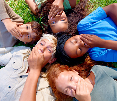Can you keep a secret. A group of children lying on the grass covering their mouths.の写真素材