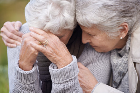 Im here to wipe your tears...An aging senior woman consoling her friend as they sit outdoors.