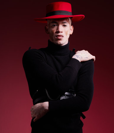 Fashion, aesthetic and portrait of man on red background with style, beauty and designer cosmetics in studio. Creative, art and male model with vitiligo pose with stylish, modern and luxury clothingの写真素材