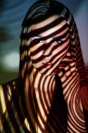 Study of light and beauty. Studio shot of a young woman with projected patterns and colors on her face.の写真素材