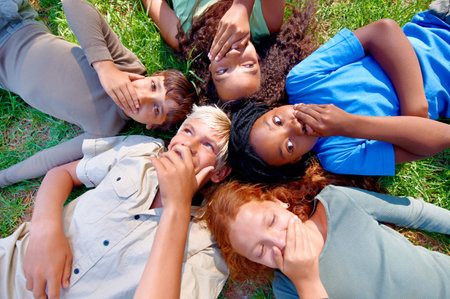 Can you keep a secret. A group of children lying on the grass covering their mouths.