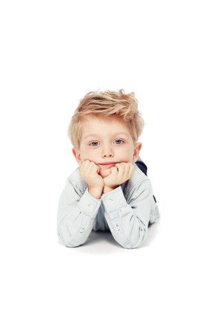 Dreaming of the big wide world...A cute little boy lying down looking at the camera - isolated.の写真素材