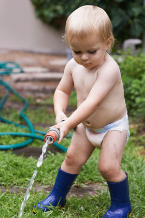 I will water the garden. A little toddler in gumboots watering the garden.の写真素材