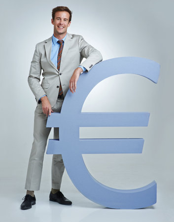 Standing strong with the Euro. Portrait of a young businessman standing alongside a Euro currency symbol.の写真素材