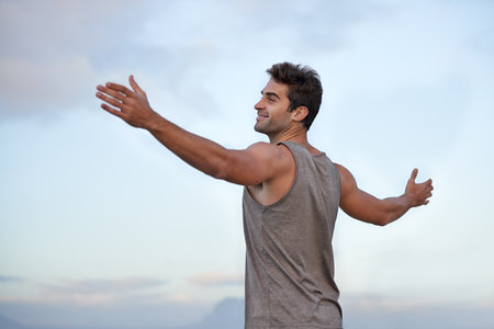 Ready to start the day. Low angle shot of a young man with his arms raised up with only the sky in the background.の写真素材