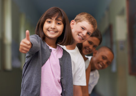 Feeling positive about school. Portrait of a young girl giving you the thumbs-up with her friends behind her.の写真素材