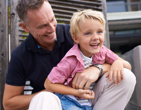Sharing a laugh with dad. a father and son sharing a laugh while sitting outs.の写真素材