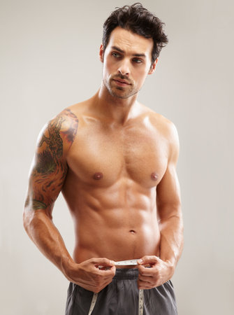 Measuring his rock hard abs. A hunky young man measuring his waist.の写真素材