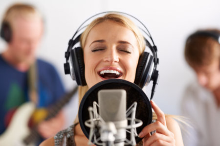 Her vocals are sure to top the charts. A beautiful young woman singing into a microphone with two band members in the background.の写真素材