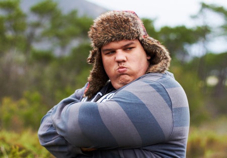 Hes got attitude. An overweight young man in a woolly cap standing with his arms folded and pursing...
