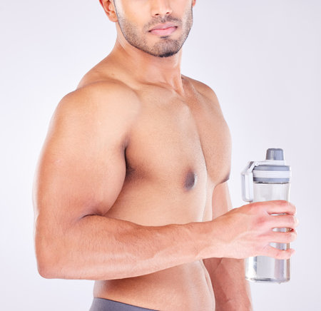 Muscle, body and man with water bottle for healthcare exercise or personal trainer. Wellness model, training or fitness strength motivation and workout with strong hands in grey studio backgroundの写真素材
