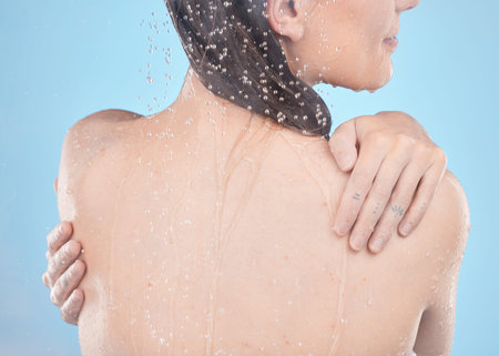 Back, woman and shower for skincare, clean and hygiene against blue studio background. Young female,...