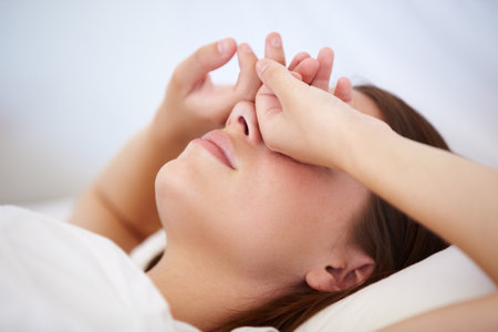 Waking up with a huge headache. A young woman lying in bed with her hands over her eyes.の写真素材