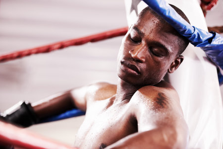 Suffering the effects of a hard bout. An exhausted young boxer leaning against the ring after a trying round.の写真素材