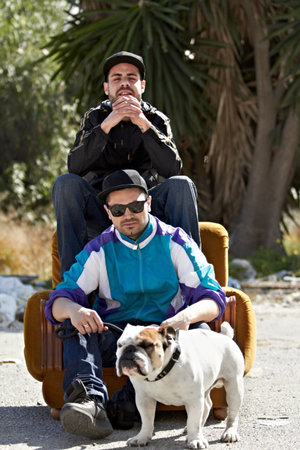 Urban lifestyle. Two gangsters sitting on a couch that is situated in the middle of a street with their dog.の写真素材