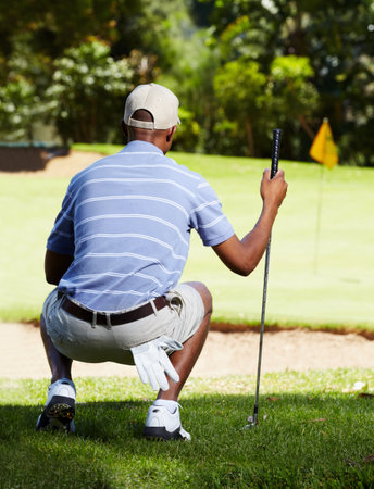 A tough chip over the bunker. Rearview shot of a golfer eyeing up a long chip to the green.の写真素材