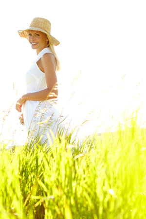 Countryside calm. An attractive young blonde woman standing in a meadow wearing a sunhat on a summers day.の写真素材