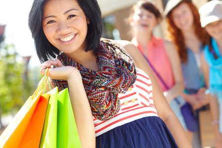 Pleased with her purchases. A beautiful ethnic girl holding shopping bags and smiling with her friends in the background.の写真素材